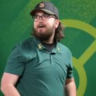 A Black man with a goatee wears a black t-shirt and is staring at the camera.